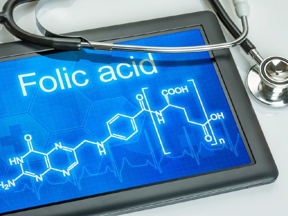 Natural Pharmaceuticals Movisan Tablet, millel on kiri „Folic acid” ja foolhappe (vitamiin B9) struktuurimuster sinisel taustal koos molekulaarvõrgustiku ja EKG-joonega; seadme peal on stetoskoop.
